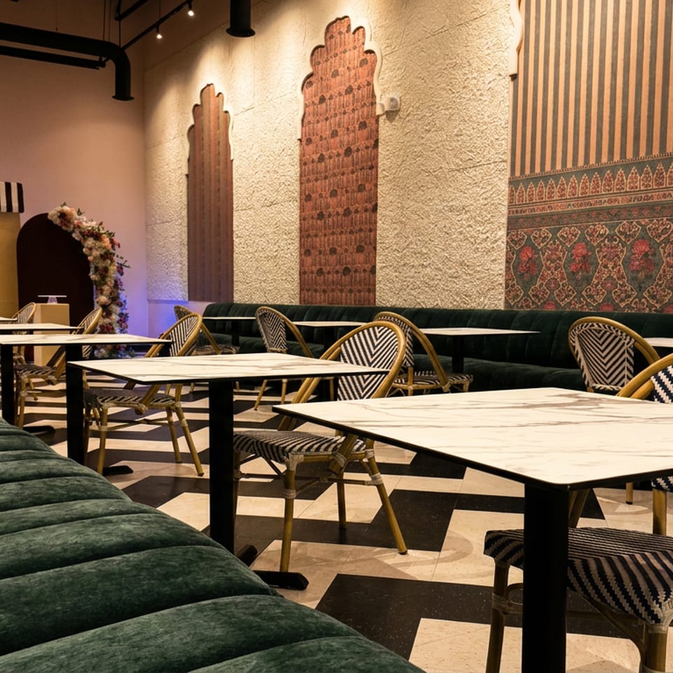 Stylish restaurant interior with emerald banquettes, patterned chairs, marble tables, geometric flooring, and colorful textured wall art.